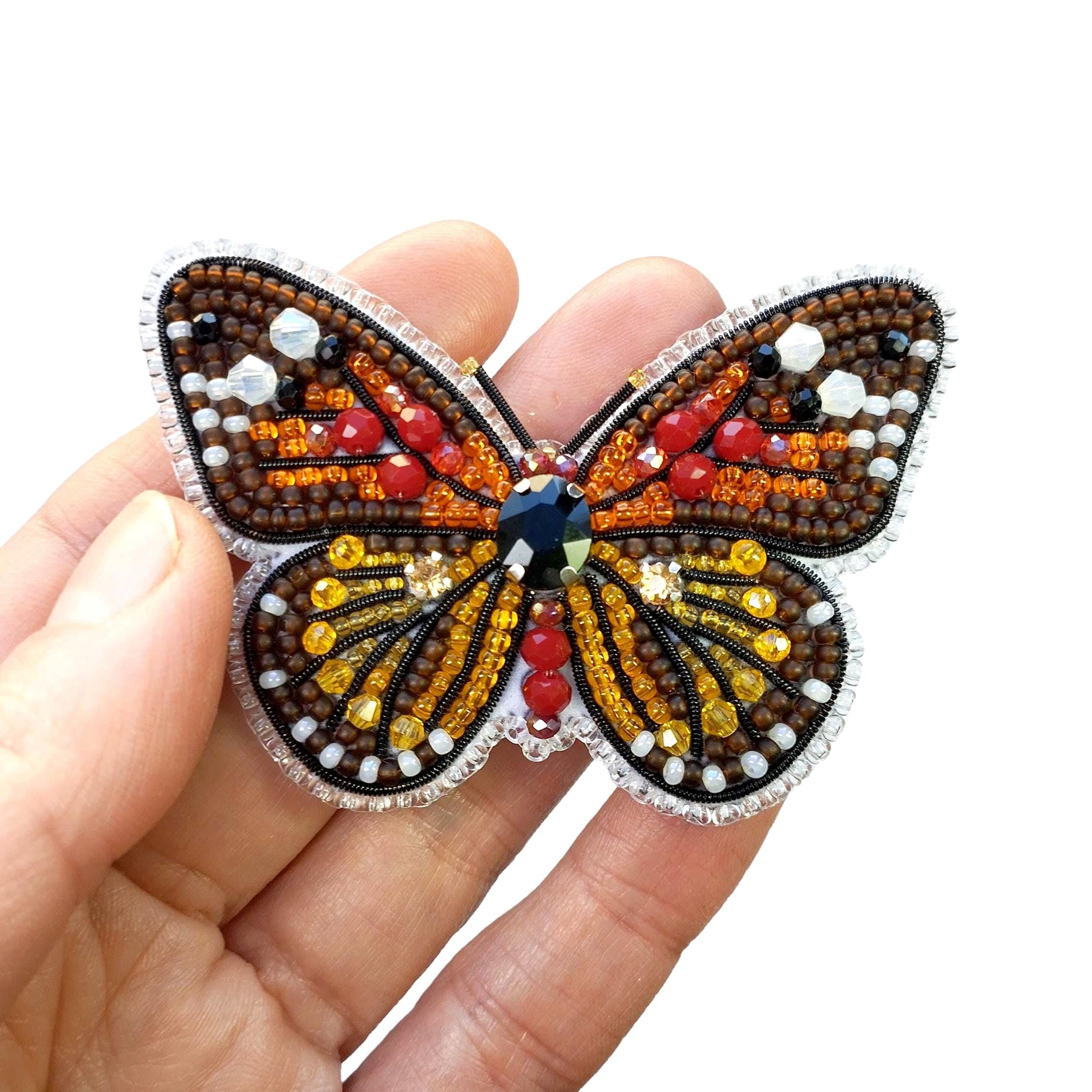 a hand is holding a beaded butterfly brooch